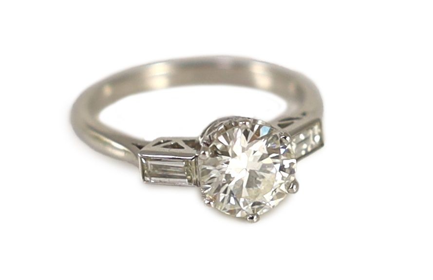 A platinum and single stone diamond ring, with baguette cut diamond set shoulders